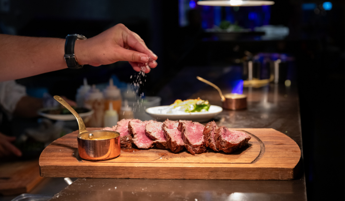 A hand sprinkling salt over steak.